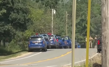 Varias camionetas azules de la policía estatal con luces encendidas en una carretera. Agentes uniformados y un poste de madera son visibles