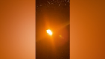 Una intensa luz naranja y amarilla brillante en el centro de una imagen oscura con pequeños puntos luminosos dispersos en la parte superior