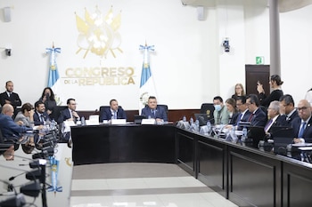 Autoridades y asistentes sentados alrededor de una mesa curva con micrófonos frente al emblema del Congreso de la República de Guatemala