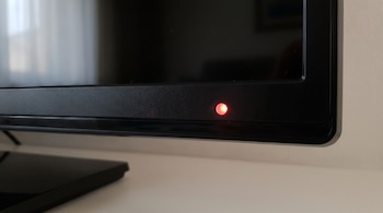 Marco inferior de un televisor de color negro con un punto de luz roja encendido en el lado derecho.