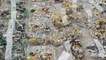 Vista superior de numerosas bolsas de plástico transparente con piezas LEGO de colores beige, verde, rojo y negro, muchas numeradas para montaje