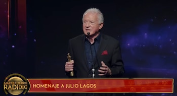 Un hombre de traje oscuro sostiene una estatuilla dorada frente a un micrófono ante una pantalla con el texto Homenaje a Julio Lagos
