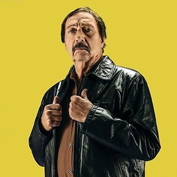 Retrato de Luis Brandoni, un hombre de mediana edad con bigote y cabello oscuro, vistiendo una chaqueta de cuero negra y una camisa marrón, contra un fondo amarillo liso