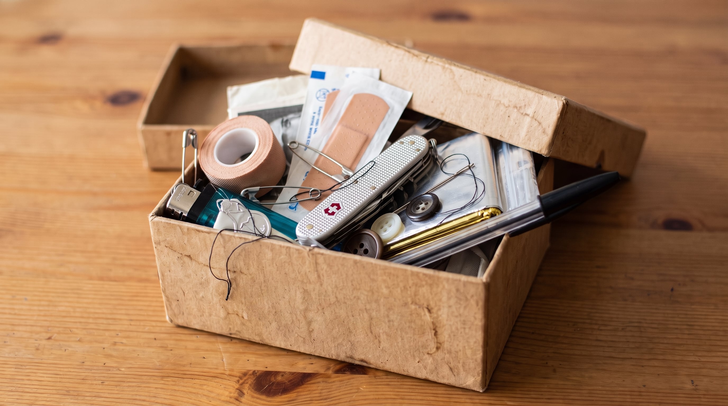 Una caja de cartón abierta reúne artículos de primeros auxilios y costura para situaciones imprevistas sobre una superficie de madera. (Imagen Ilustrativa Infobae)