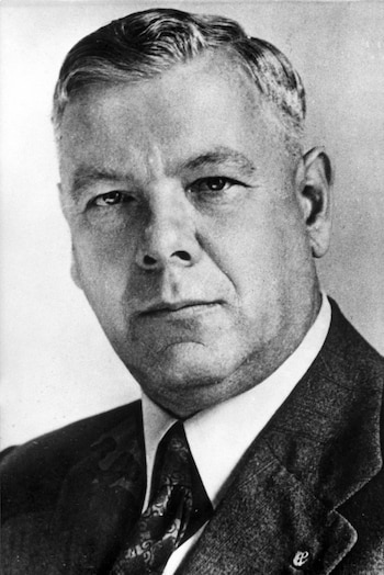 Retrato en blanco y negro de Hendrik Frensch Verwoerd, un hombre de mediana edad con cabello peinado hacia atrás, traje y corbata, mirando al frente