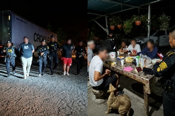 Policías armados escoltan a dos hombres esposados ante un camión de carga mientras otros agentes vigilan una mesa con personas sentadas.
