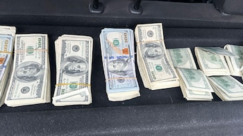 Varios fajos de billetes de cien dólares estadounidenses, tanto de diseño antiguo como moderno, atados con bandas elásticas y colocados sobre una superficie de tela oscura