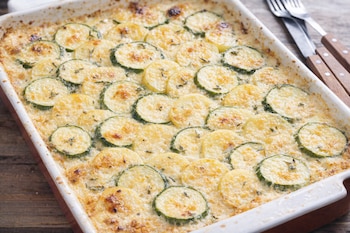 Un pastel gratinado con rodajas de calabacín y patata en una fuente.