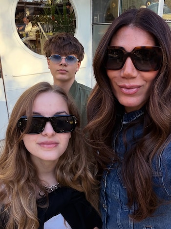 Tres personas posan para un autorretrato en el exterior; la mujer y la joven llevan gafas de sol oscuras y el joven gafas de lente azul