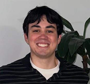 Retrato de un joven con cabello oscuro y una camisa polo a rayas, sonriendo ligeramente frente a un fondo claro con una planta verde
