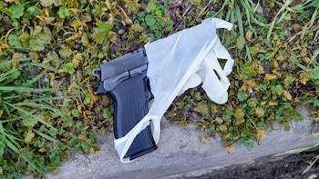 Una pistola negra cubierta en parte por un guante de látex blanco descansa sobre césped y un borde de cemento