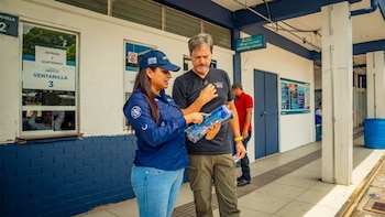 Mujer con uniforme azul y gorra con logo "Guatemala" asiste a hombre. Ventanilla con cartel "ENTRADA A GUATEMALA". Rótulo "Migración Immigration"