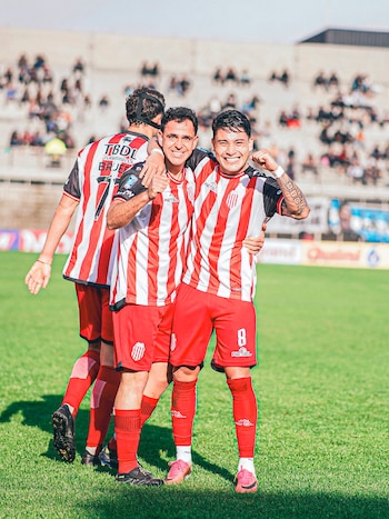 Tres jugadores de fútbol con camisetas a rayas rojas y blancas, pantalones cortos rojos y medias rojas en un campo de césped verde con tribunas
