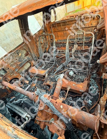 Interior calcinado y oxidado de un automóvil con armazones metálicos de asientos, restos de cables quemados y escombros en el suelo