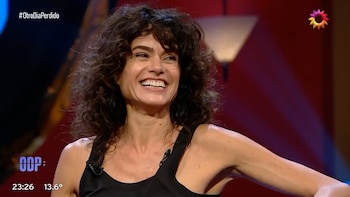Una mujer de cabello oscuro rizado y camiseta negra sonríe frente a la cámara en un estudio de televisión