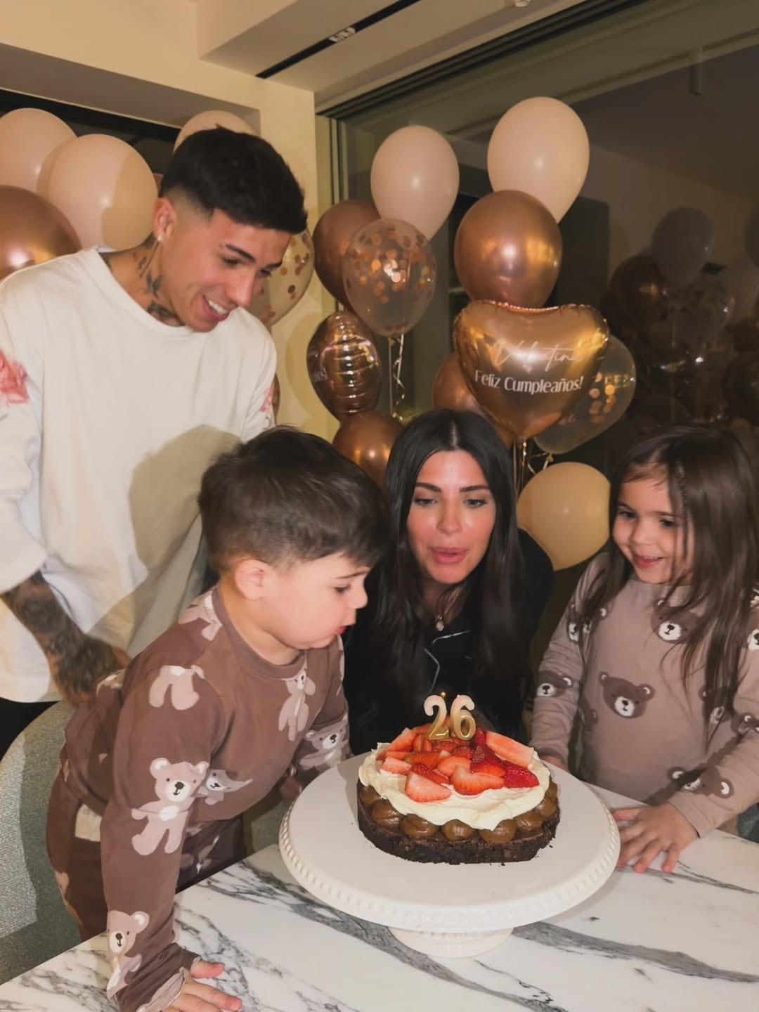 Valen Cervantes sopla las velas de una torta de chocolate y frutillas mientras sus dos hijos y su pareja, Enzo Fernánez, observan en una celebración de cumpleaños (Instagram: valucervantes)