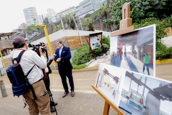 Un acantilado rocoso, una grúa amarilla de construcción, edificaciones en obra, una carretera, palmeras, vehículos y personas