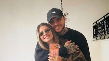 Una mujer con gafas de sol sostiene un teléfono móvil frente a un espejo junto a un hombre con gorra negra y tatuajes en la mano