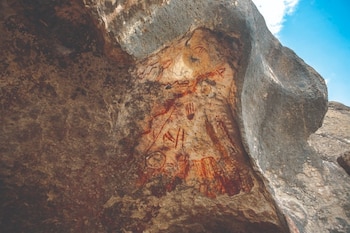 Vista del arte rupestre de Cueva Pinta con figuras rojas y anaranjadas pintadas sobre la roca de un abrigo natural, bajo un cielo azul
