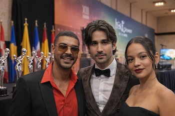 Manuel Medrano, Carlos Torres y Natalia Reyes sonríen. Se ven premios plateados y banderas nacionales en el fondo. Medrano lleva gafas de sol.