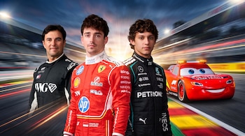 Tres pilotos con indumentaria deportiva posan junto a un vehículo rojo de ficción en una pista de carreras al atardecer.