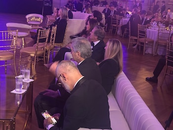 Personas vestidas con traje formal sentadas en un sofá blanco en un salón de eventos con iluminación violeta