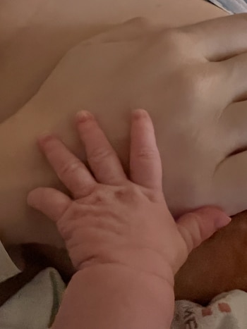 Primer plano de una mano pequeña de bebé con los dedos extendidos que se apoya sobre la palma de una mano adulta
