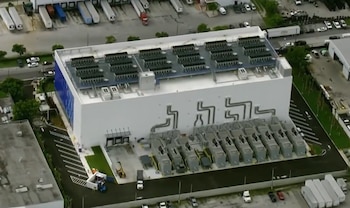 Vista aérea de un edificio industrial blanco con equipos de refrigeración en el techo y maquinaria externa