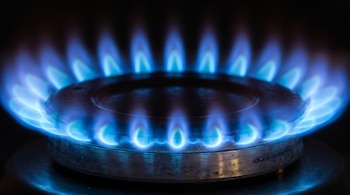 Primer plano de un quemador de estufa de gas con múltiples llamas azules sobre un fondo negro.