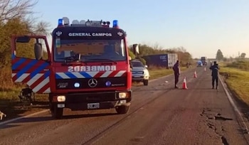 Un camión de bomberos rojo estacionado en la banquina de una ruta asfaltada junto a conos de señalización y personal de seguridad