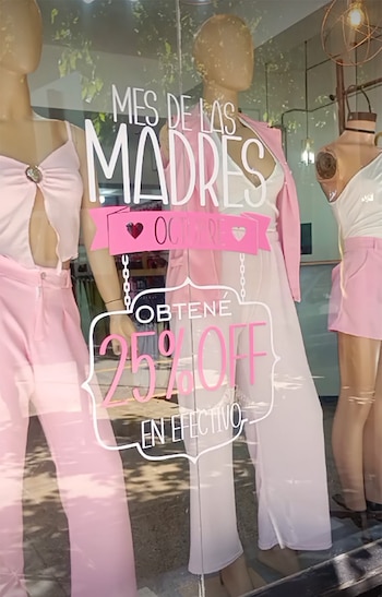 Tres maniquíes con ropa de color rosa tras el cristal de una tienda con un cartel que anuncia un descuento del 25 por ciento en efectivo