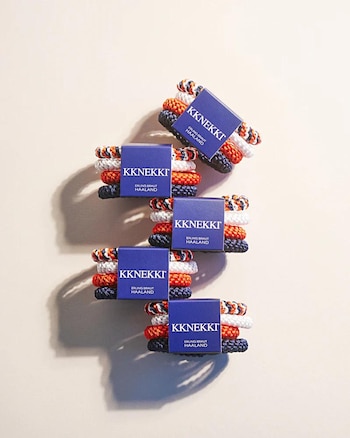 Cinco paquetes de gomitas para el pelo marca KKNEKKI con tres unidades cada uno, en colores naranja, azul marino y blanco estampado, dispuestas en diagonal