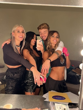 Cuatro jóvenes, tres mujeres y un hombre, posan sonrientes para una selfie en un espejo; una mujer lleva un guante rosa con pinchos