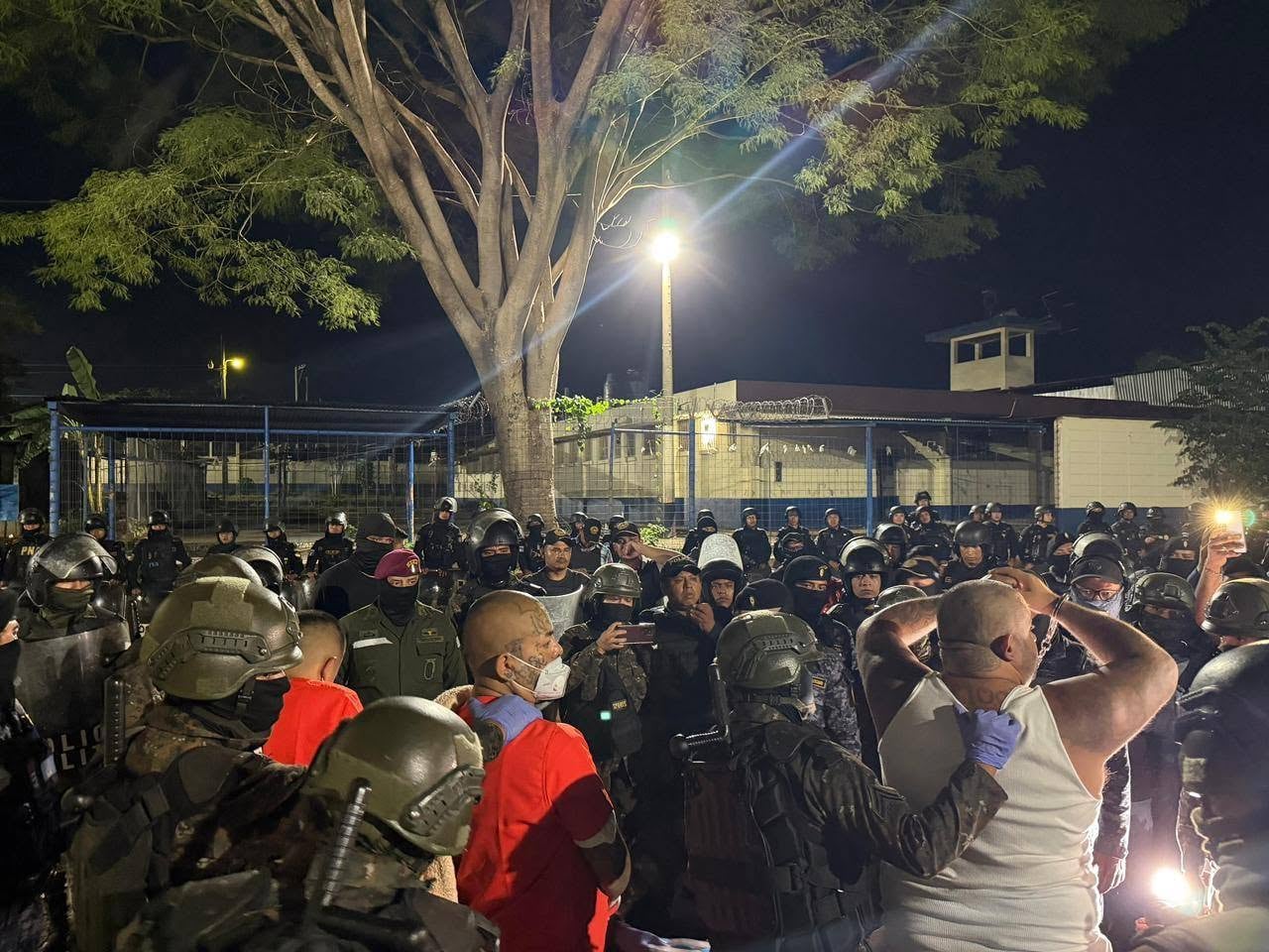 Un grupo de agentes de seguridad custodia a varios hombres esposados durante un despliegue nocturno en las afueras de un centro de detención. (Dirección General del Sistema Penitenciario de Guatemala)