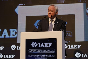 Un hombre de cabello gris, vestido con traje y corbata, habla en un atril con dos micrófonos. El atril muestra el logo 'IAEF 43° Congreso Anual'. Detrás, una gran pantalla
