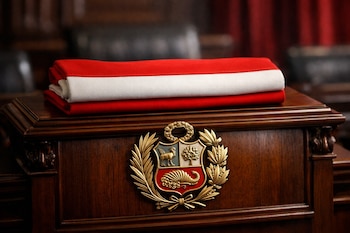 Atril de madera pulida con escudo nacional metálico y una banda de tela doblada con franjas roja y blanca en un salón interior.