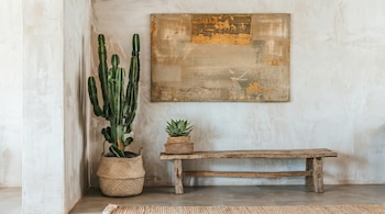 Un cactus alto en una cesta de mimbre, un banco de madera y una planta suculenta en un macetero sobre él, con un cuadro abstracto en la pared.