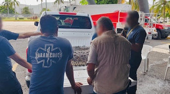 Varias personas observan a un cocodrilo sujetado con cuerdas en la caja abierta de una camioneta blanca.