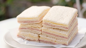Sándwiches de pan de molde sin corteza con jamón y queso, apilados en dos filas sobre un plato blanco.