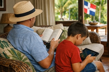 Un adulto con sombrero de paja lee un libro, junto a un niño que mira una tableta. Se ve la bandera de República Dominicana por la ventana.
