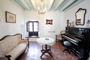Sala con sofá, mesa octogonal de madera, piano vertical, espejo de pared, lámpara de araña, cuadros, ventana con contraventanas de madera