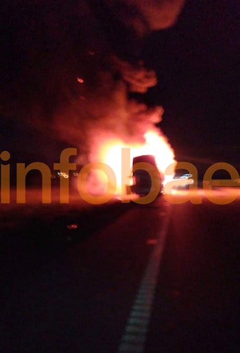 Un micro de pasajeros en llamas en una ruta oscura durante la noche, con grandes columnas de fuego y humo anaranjado y rojo. El logo de Infobae es visible