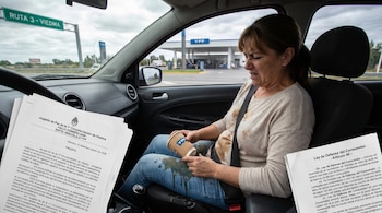 Mujer en el asiento de un coche con café derramado en su regazo y ropa; al fondo, una estación de servicio YPF y un cartel de "Ruta 3 - Viedma". Documentos legales superpuestos.