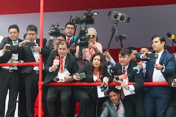 Grupo de periodistas con cámaras, micrófonos y teléfonos móviles detrás de una valla roja, en un evento al aire libre