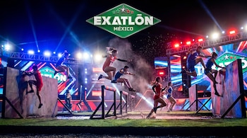 Vista panorámica de atletas saltando y corriendo en una pista de obstáculos acuática e iluminada, con el logo de Exatlón México y pantallas LED al fondo.