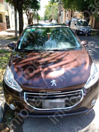 Automóvil Peugeot 208 de color marrón oscuro estacionado al borde de una calle. Se observan árboles, edificios y otros vehículos en el fondo