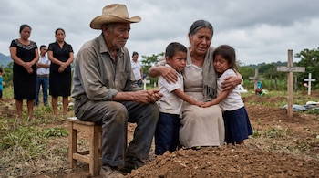Hombre anciano con sombrero sentado y mujer mayor llorando abrazando a dos niños en un cementerio, con montículos de tierra y cruces de madera en el fondo.