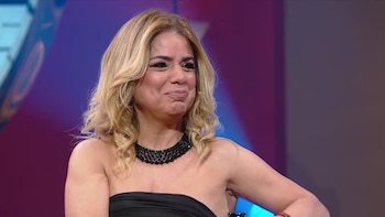 Marina Calabró realiza un gesto facial mientras luce un collar negro y un vestido oscuro en un estudio de televisión