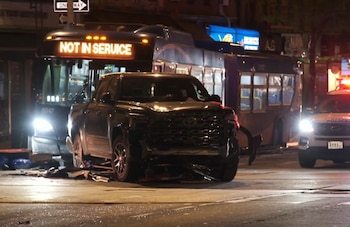Un autobús de la MTA "NOT IN SERVICE" y una camioneta negra destrozada tras un accidente nocturno en Manhattan. Hay escombros en la calle y un coche de policía visible