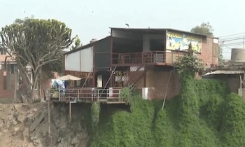 Un inmueble de dos niveles con un cartel de cebichería se ubica al borde de un terreno erosionado cubierto de vegetación